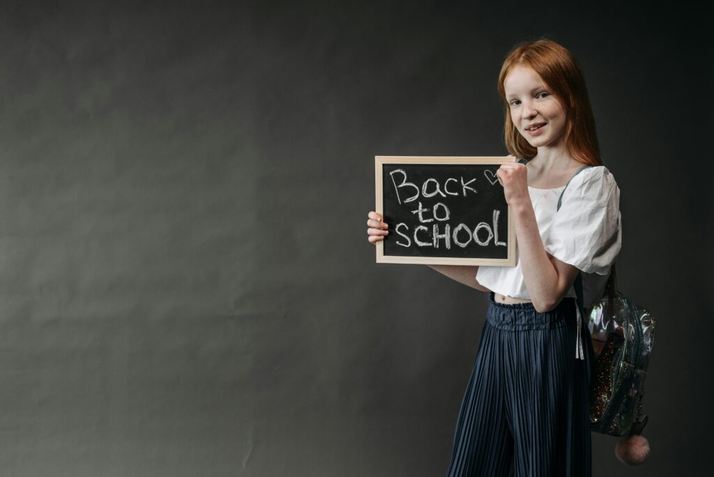 Young girl holding a 'Back to School' chalkboard, ready for the school year.